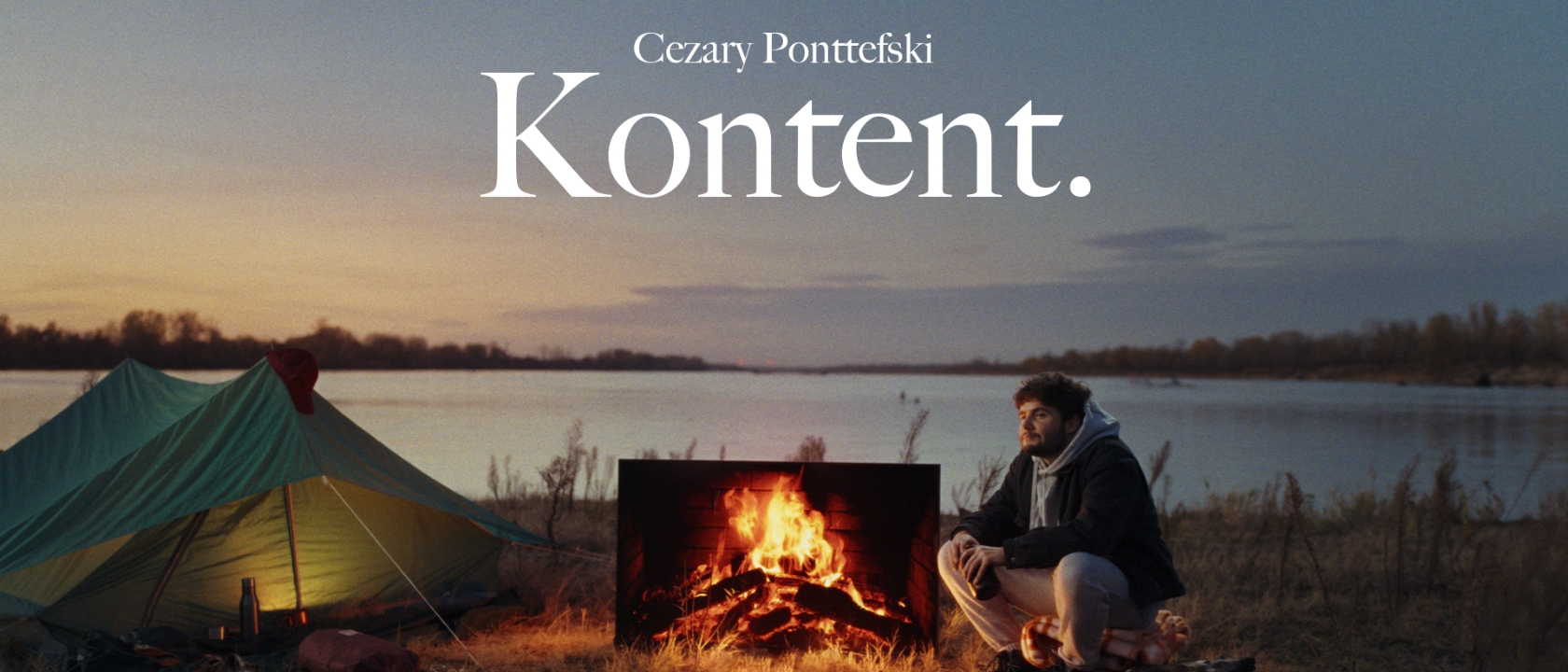 zdjęcie przedstawia mężczyznę siedzącego nad ogniskiem nad rzeką - na górze nad jego głową napis: 