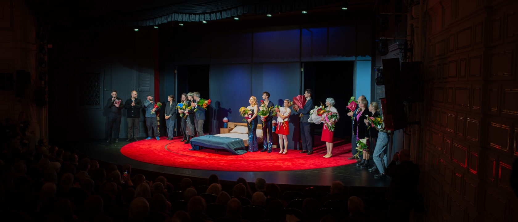 na zdjęciu aktorzy na scenie z kwiatami, stoją do braw