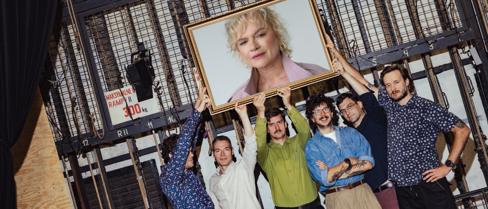 na zdjęciu kilku śmiejących się mężczyzn z Teatru Klancyk trzyma ramę obrazu, w ramie widać zdjęcie aktorki Katarzyny Figury