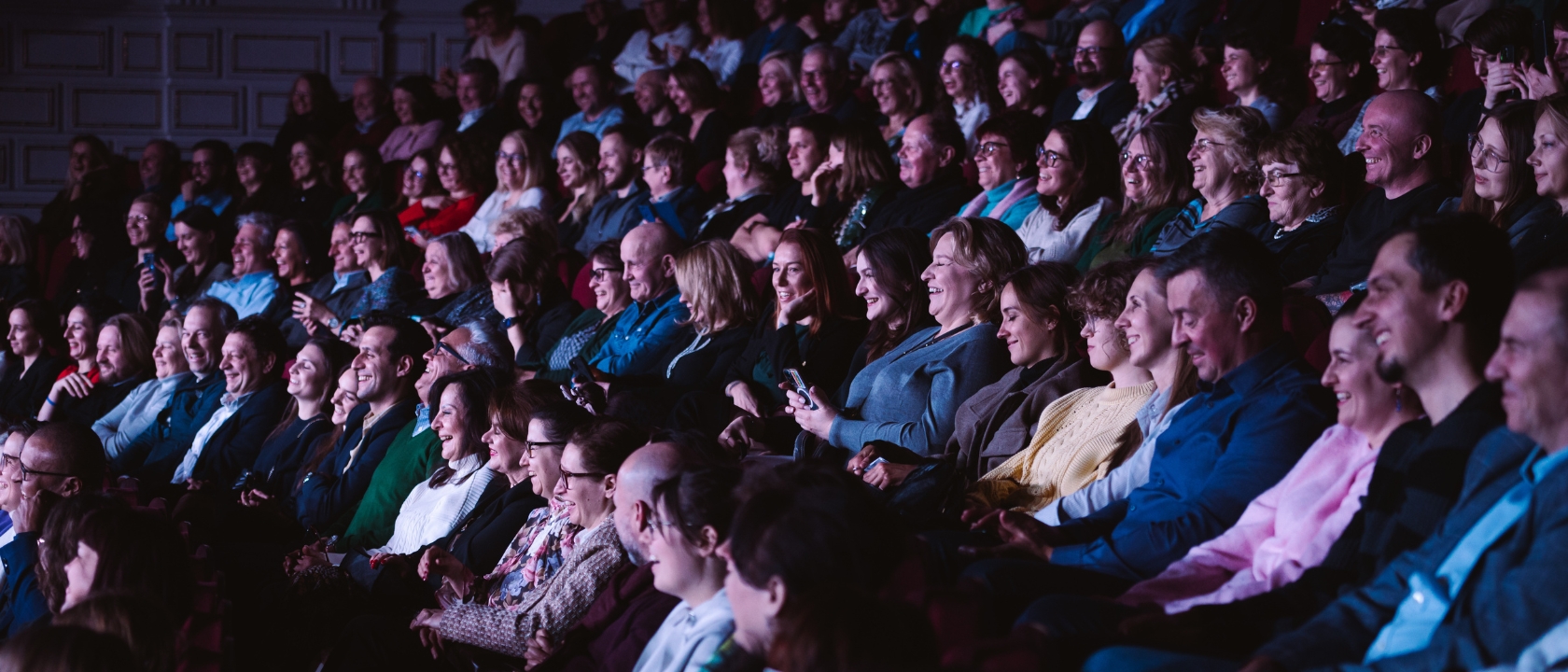 Zdjęcie przedstawia widownię Teatru Komedia, sala teatralna jest pełna ludzi w różnym wieku czekających na rozpoczęcie przedstawienia